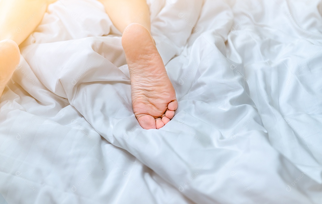 Mulher com os pés descalços na cama sobre o cobertor de linho branco