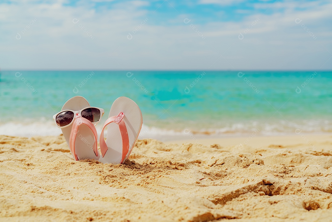 Sandálias rosa e brancas, óculos de sol na praia de areia à beira-mar.