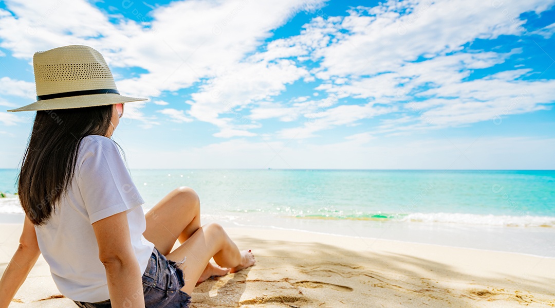 Mulher jovem feliz em camisas brancas e shorts sentado na praia de areia