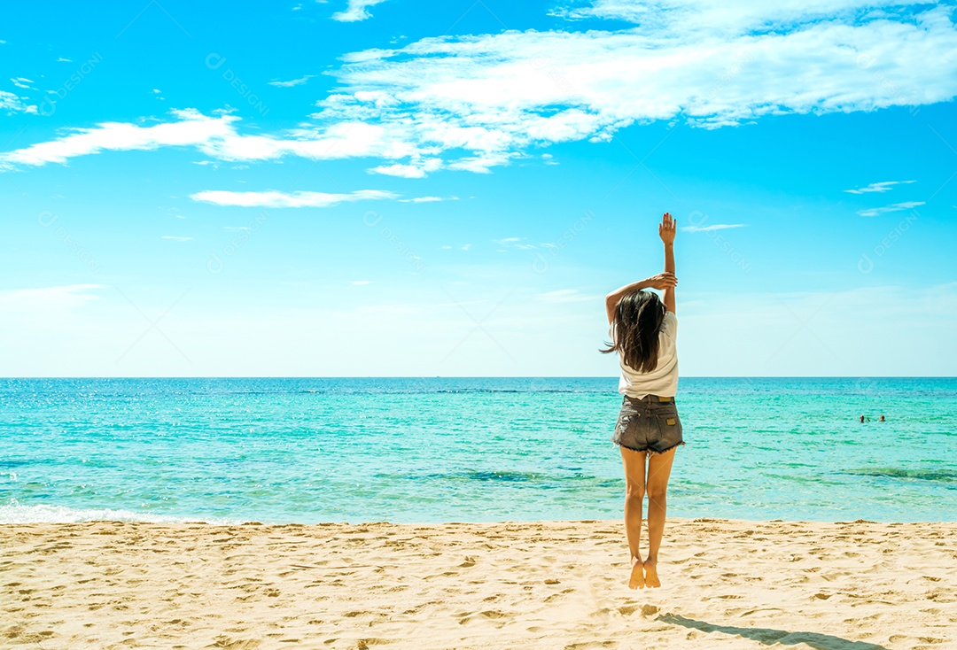 Mulher jovem feliz em camisas brancas e shorts pulando na praia de areia
