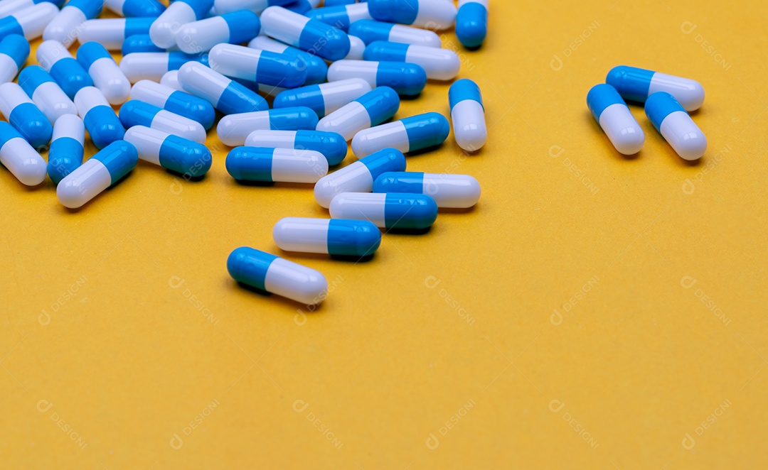 Comprimidos de cápsulas de antibióticos azuis e brancos espalhados em fundo amarelo
