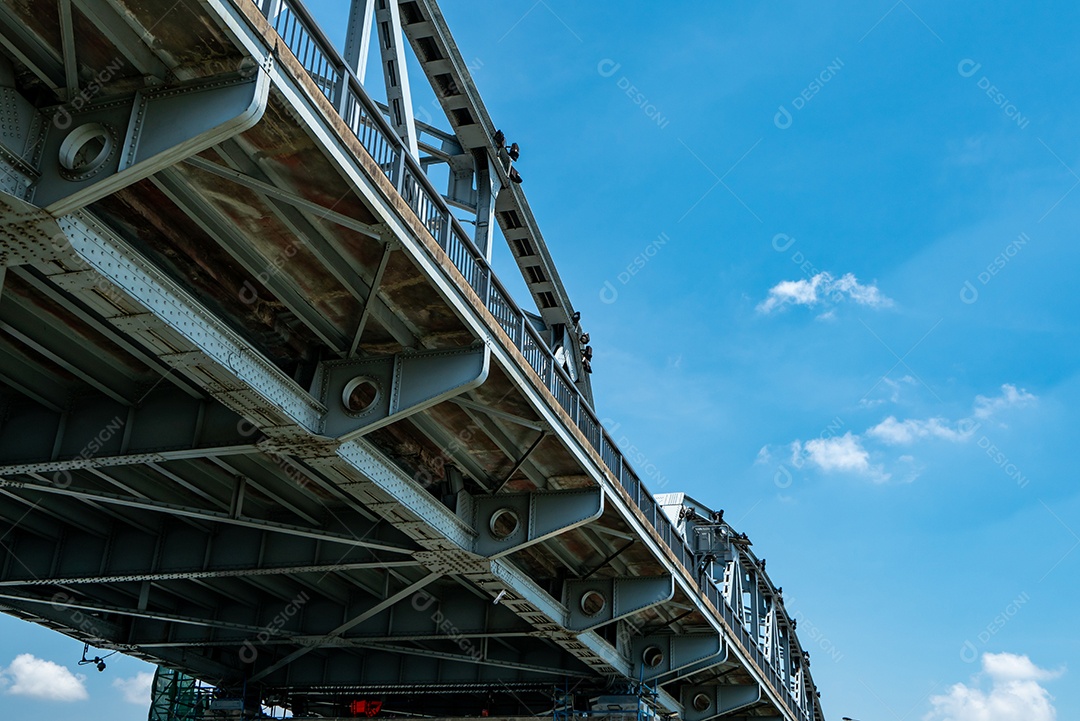 Estrutura de ponte de aço contra céu azul e nuvens brancas.