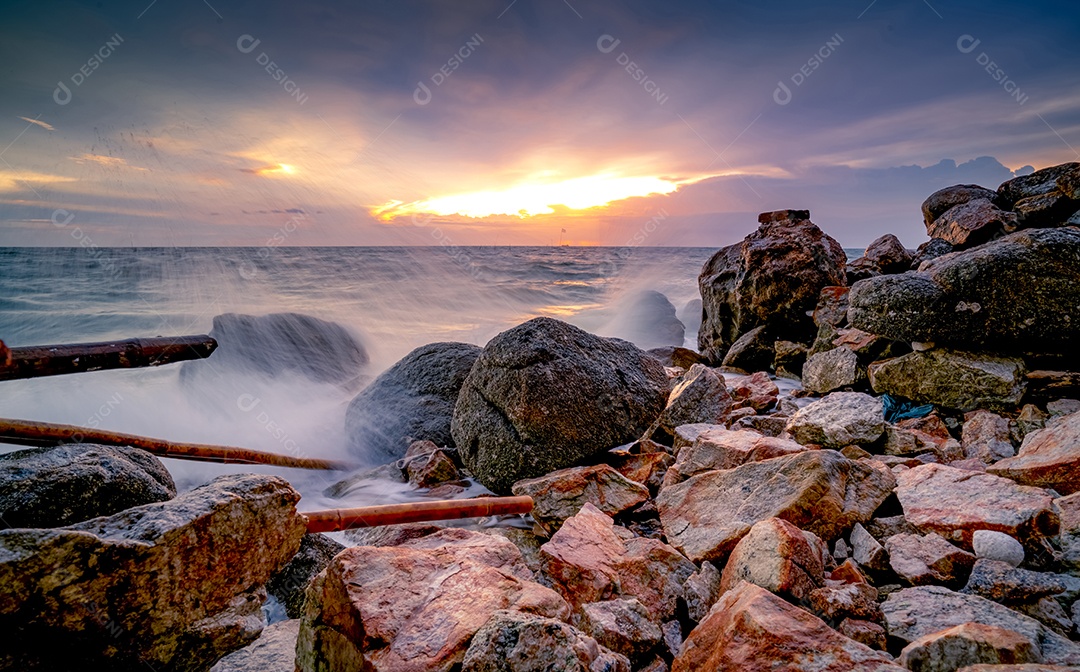 Respingos de água do oceano na praia rochosa com lindo céu pôr do sol