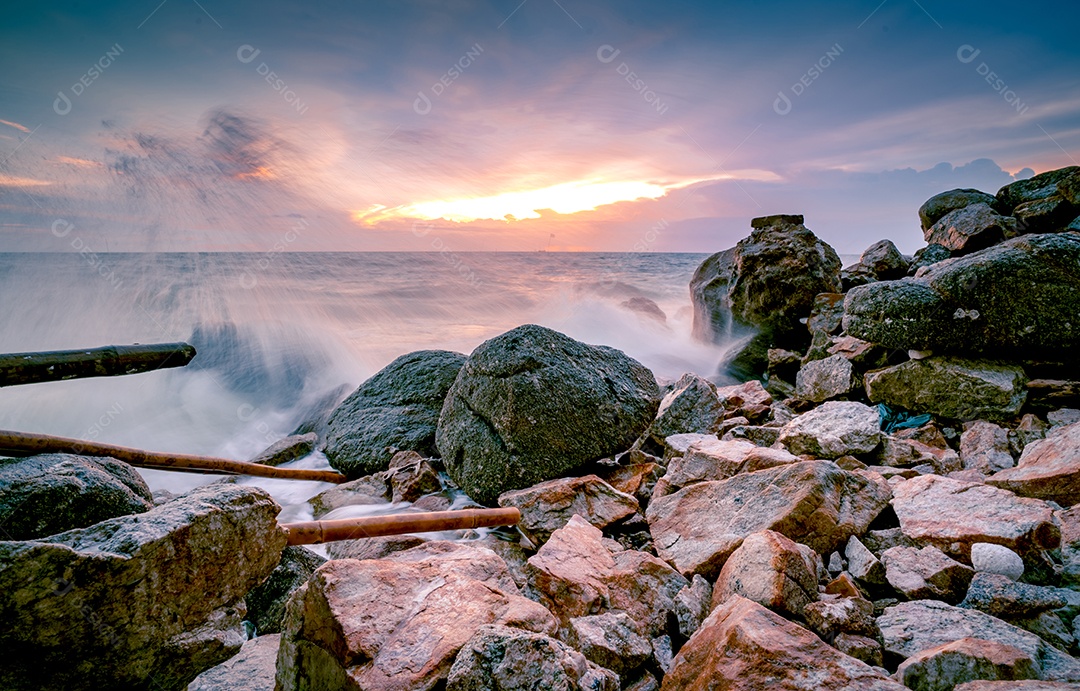 Respingos de água do oceano na praia rochosa com lindo céu pôr do sol