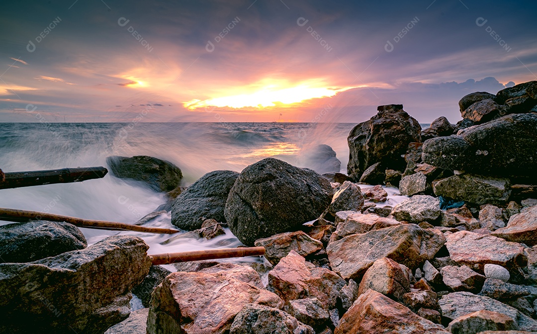 Respingos de água do oceano na praia rochosa com lindo céu pôr do sol