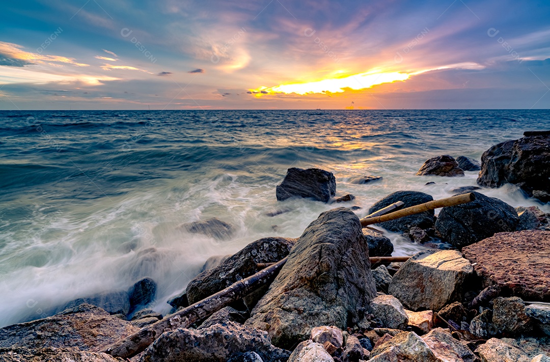 Respingos de água do oceano na praia rochosa com lindo céu pôr do sol