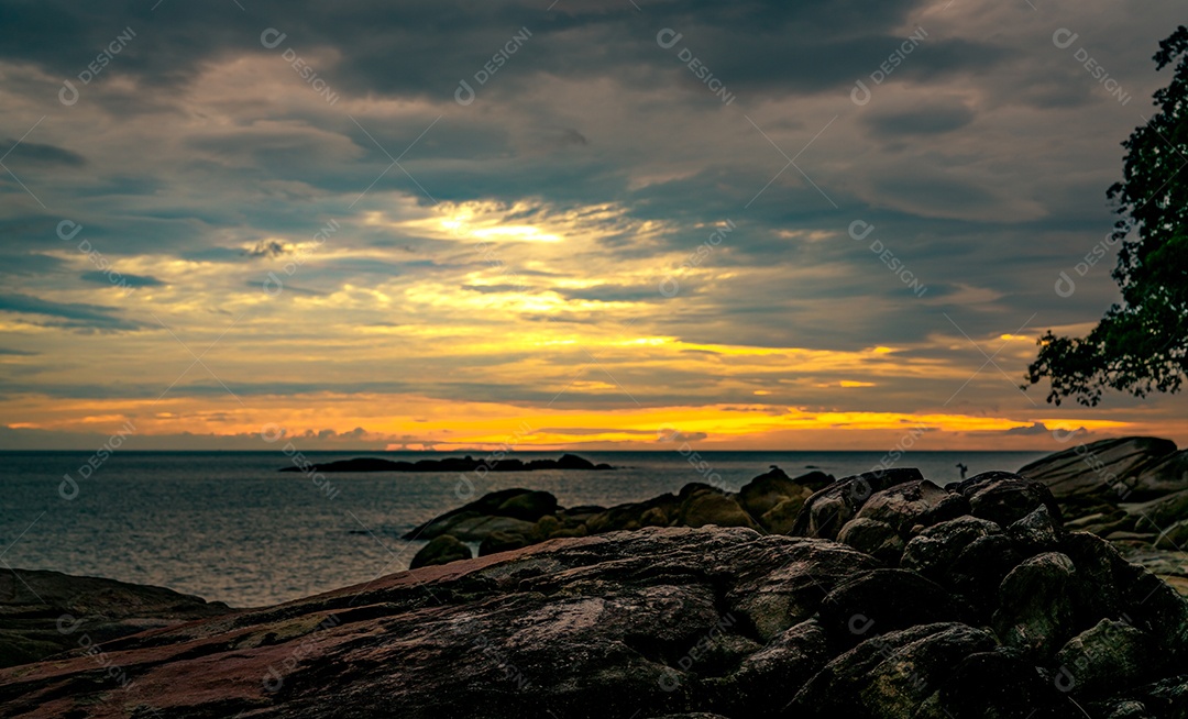 Bela praia de pedra pela manhã com o céu dourado do nascer do sol.