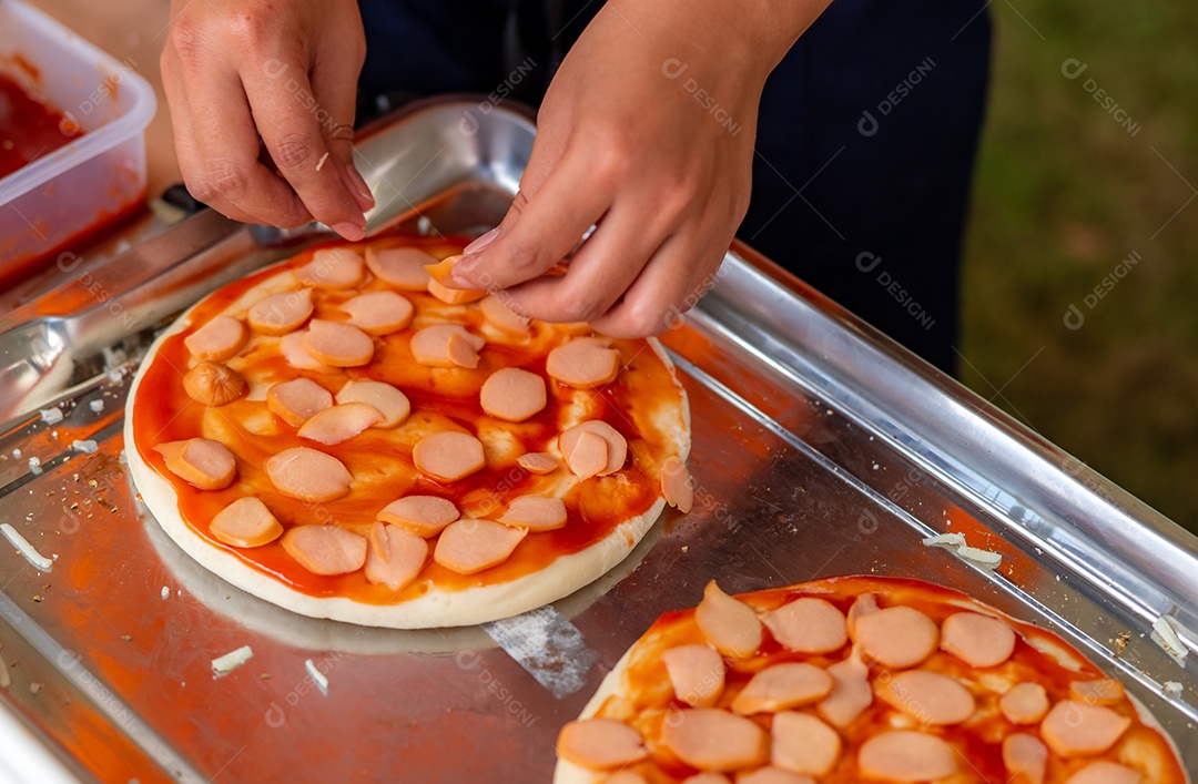 Homem faz pizza na cozinha com massa de pizza e linguiça fatiada.