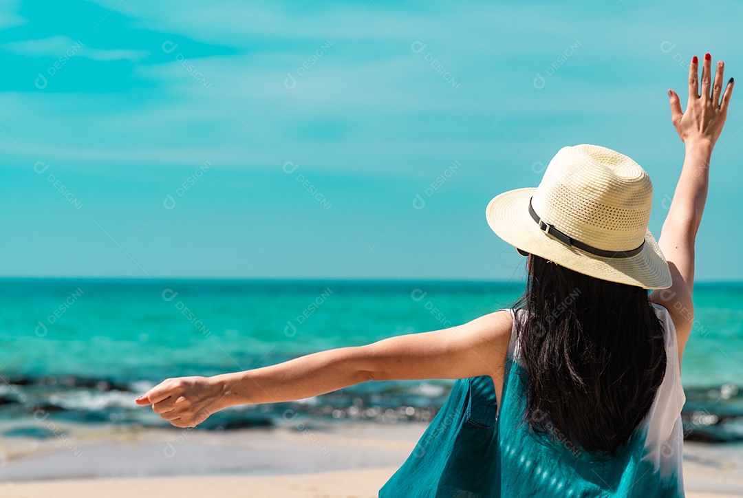 Uma jovem feliz usa chapéu de palha, senta e levanta a mão na praia de areia