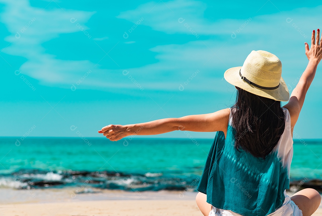 Uma jovem feliz usa chapéu de palha, senta e levanta a mão na praia de areia