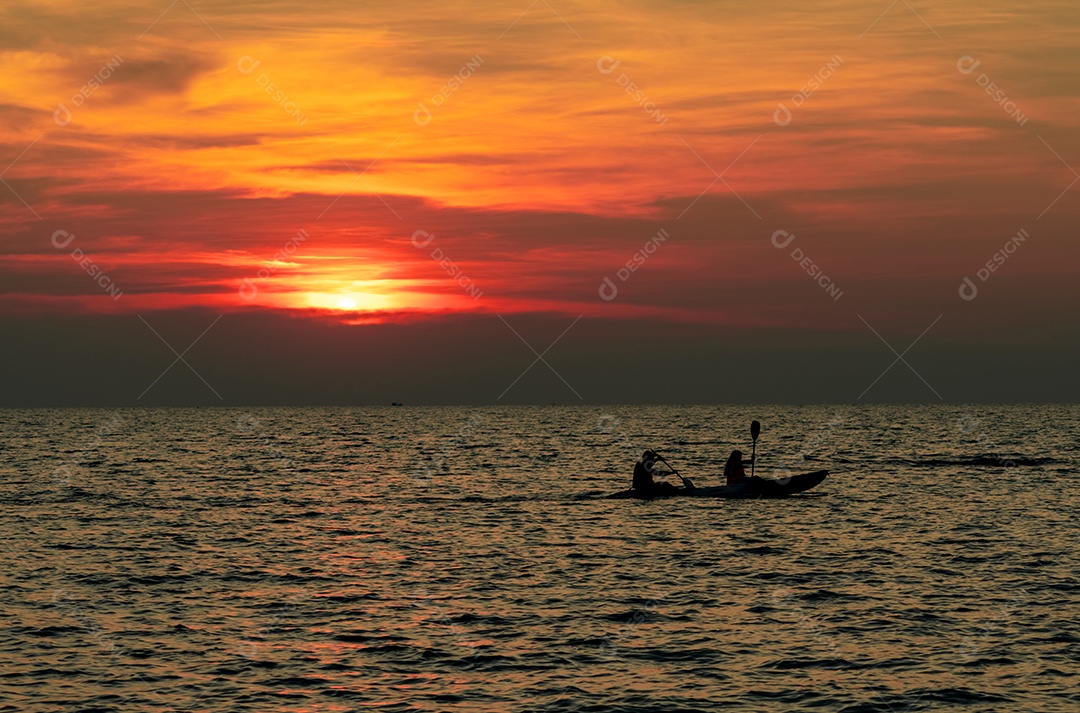 A silhueta do casal está andando de caiaque no mar ao pôr do sol.