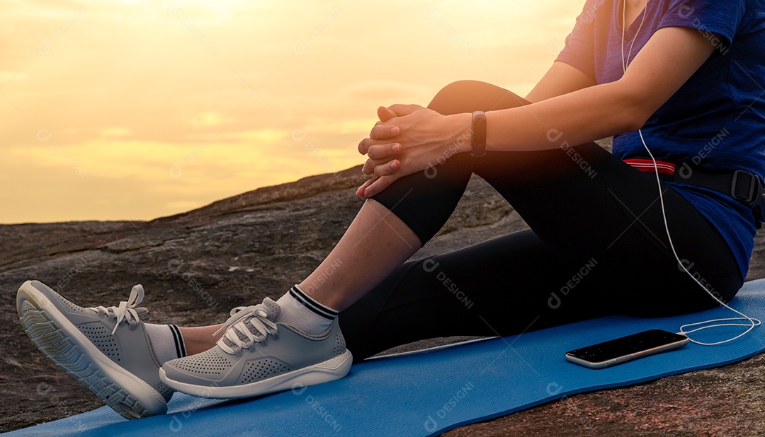 A mulher senta e relaxa no tapete de ioga e ouve música via smartphone