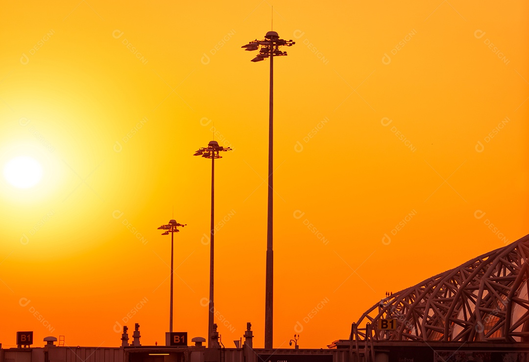 Pilão elétrico alto no aeroporto ao pôr do sol com um céu laranja.