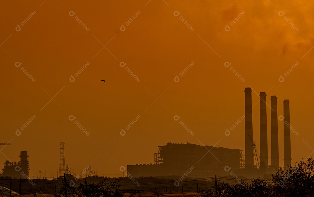 Usina com céu pôr do sol laranja e pássaros voando no céu.