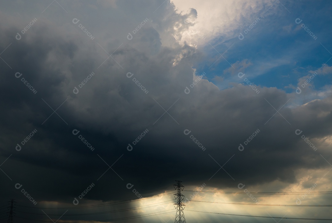 Céu azul e nuvens cinzentas com luz solar branca acima de alta tensão