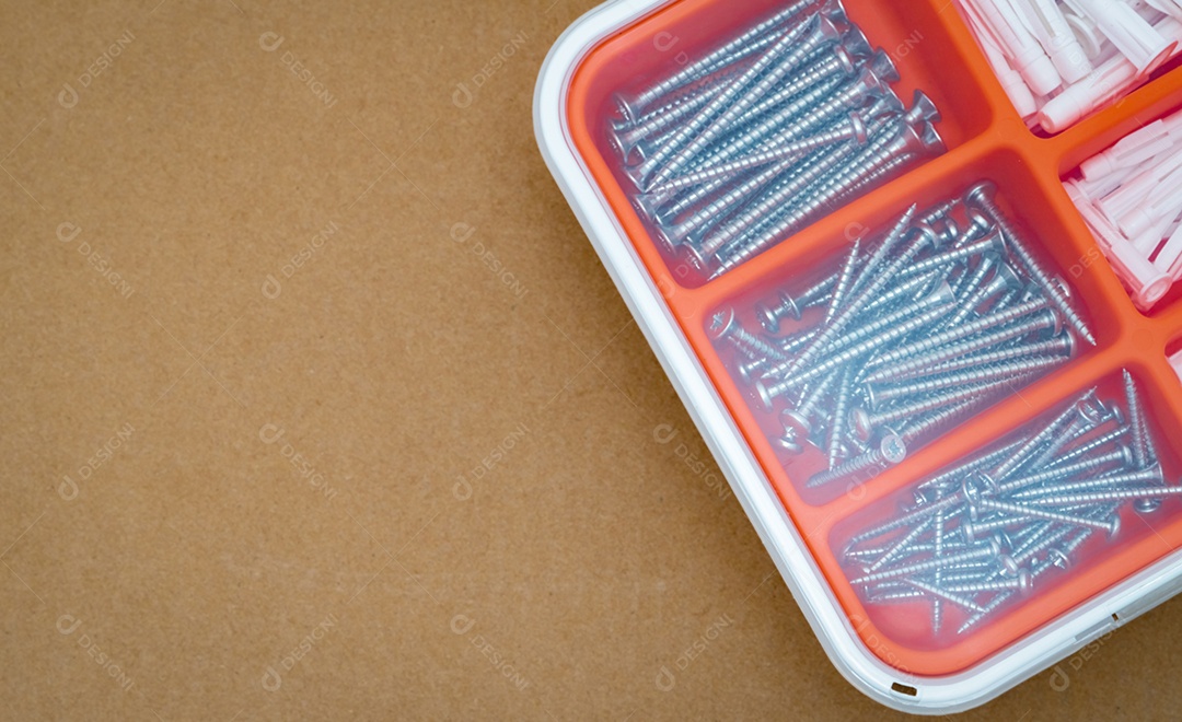 Parafusos de aço prateado e bucha em caixa de plástico laranja.