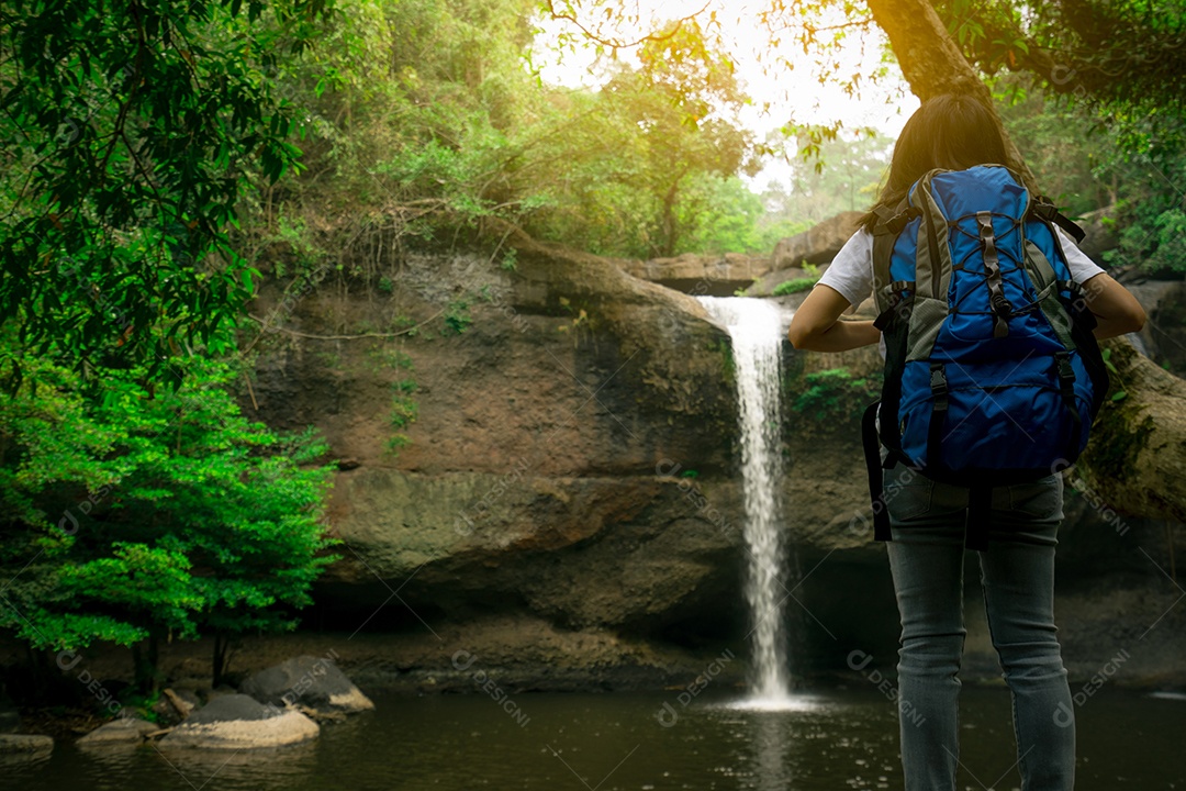 Vista traseira da mulher asiática com mochila observando pequena cachoeira