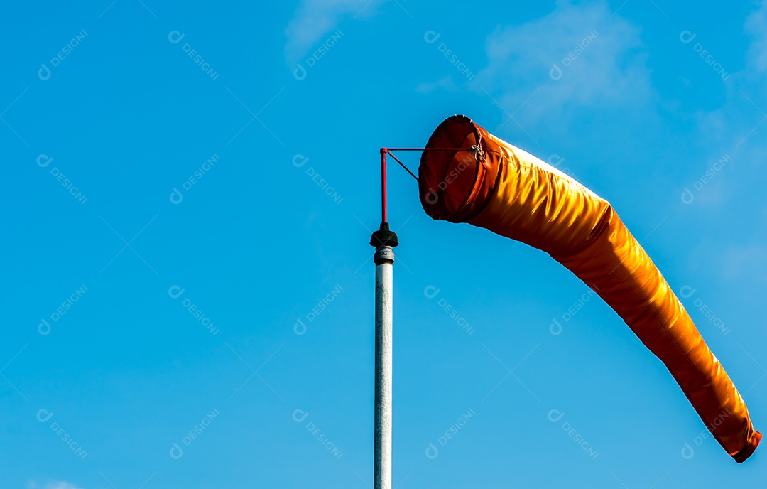Biruta laranja em vento moderado no poste branco contra azul claro