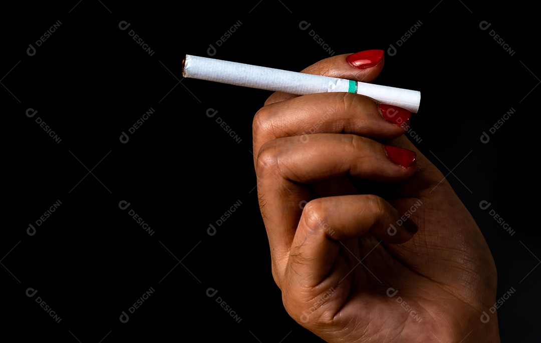 Cigarro na mão de uma mulher com unha vermelha isolada em fundo preto
