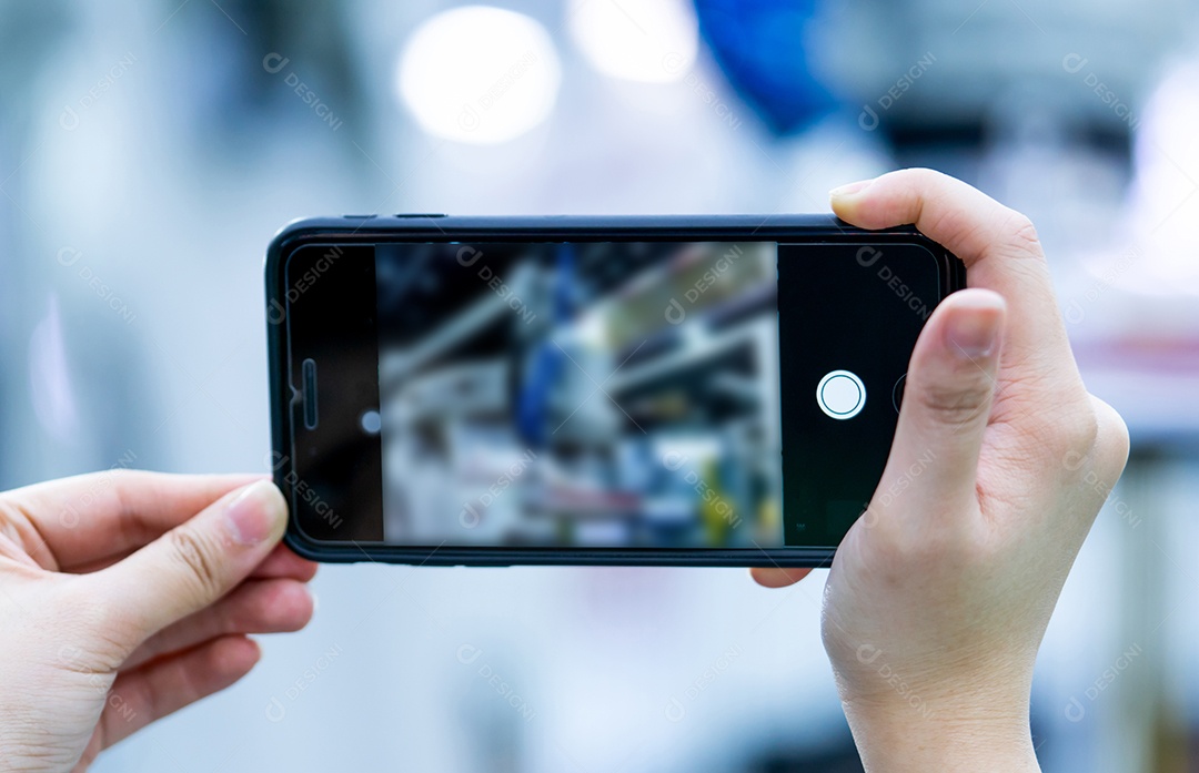A mão da mulher usa o telefone inteligente para filmar a foto do robô na industria