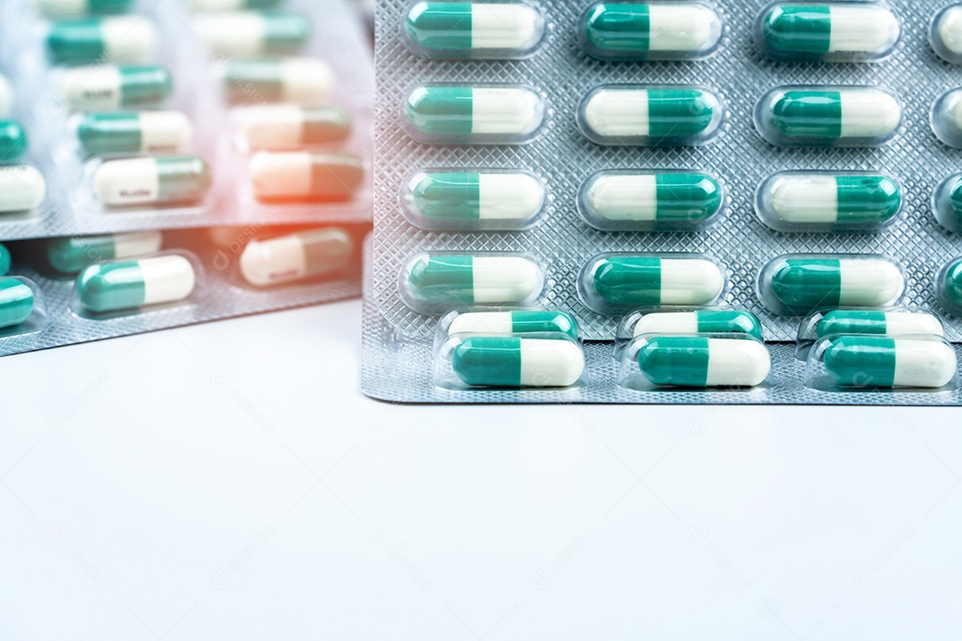 Comprimidos de pequenas cápsulas verdes-brancos em blisters na mesa branca