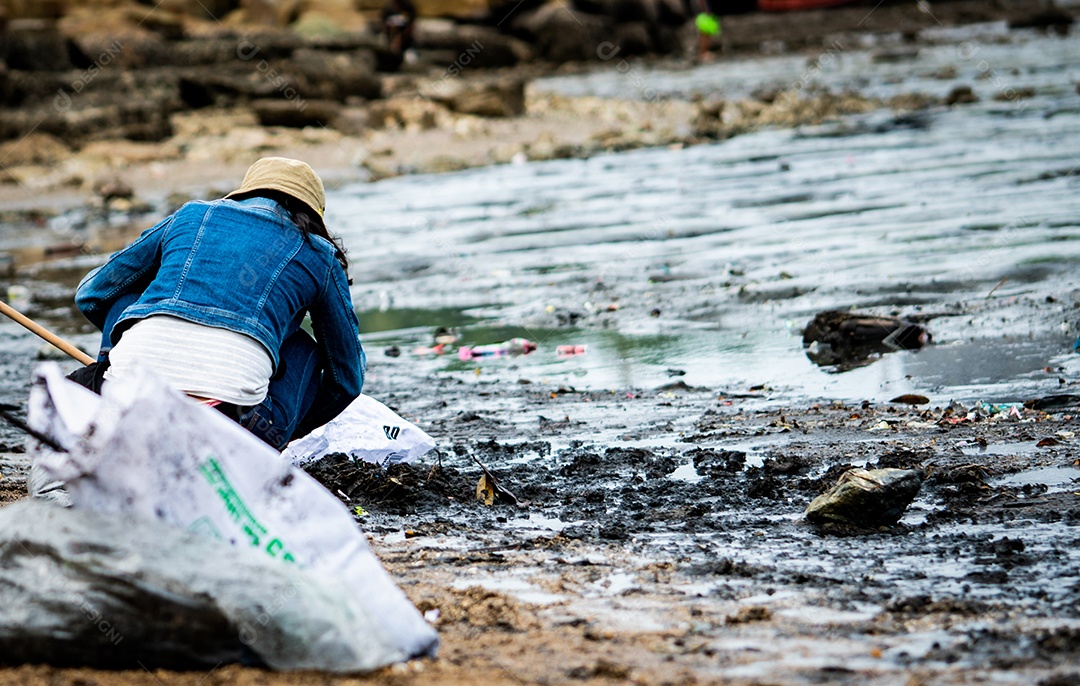 Voluntários sentam e pegam lixo na praia. limpeza de praia