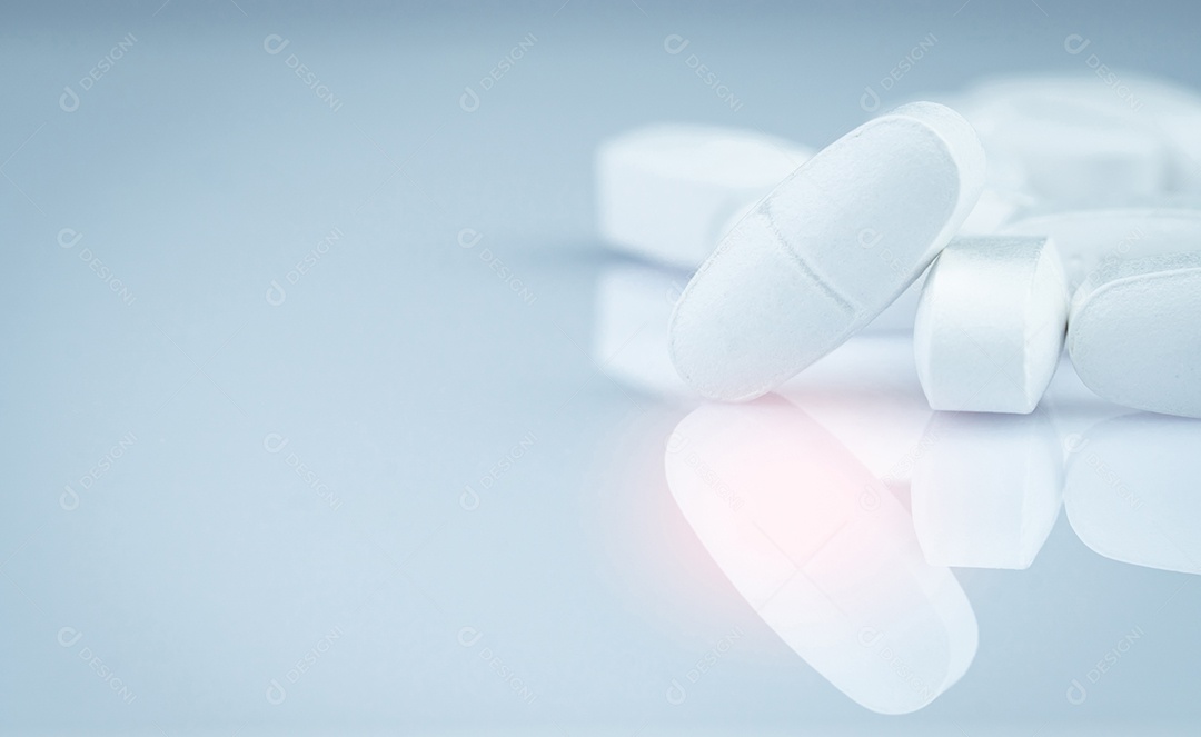 Pilha de comprimidos comprimidos oblongos brancos sobre fundo cinza.