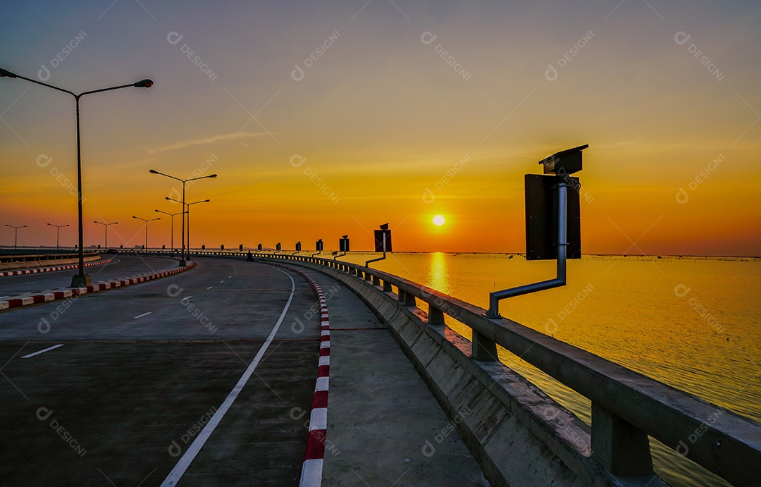 Estrada costeira curvada com lâmpada de rua e céu laranja ao pôr do sol