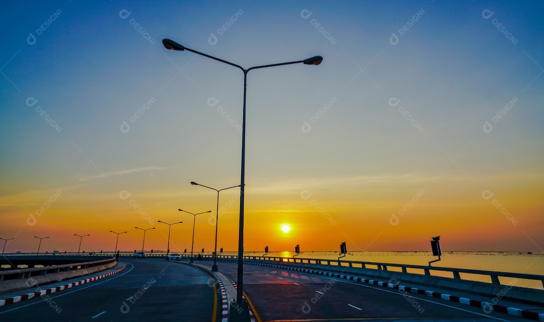 Estrada costeira curvada com lâmpada de rua e céu laranja ao pôr do sol