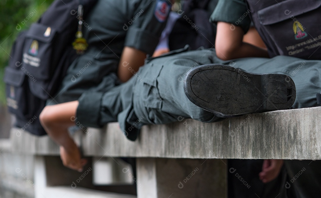 Alunos usam uniforme de estudantes militares dormindo em um banco feito de cimento