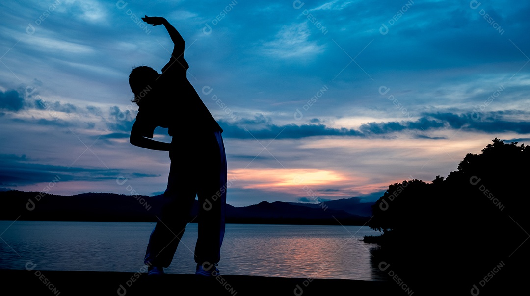 A silhueta de uma mulher se exercitando na beira de um reservatório atrás da montanha