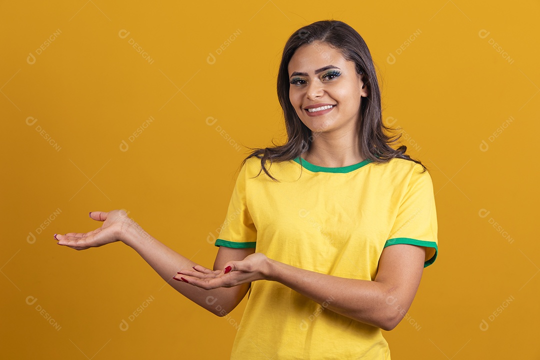 Linda mulher jovem brasileira garota torcedora do brasil fundo amarelo apontando para lado