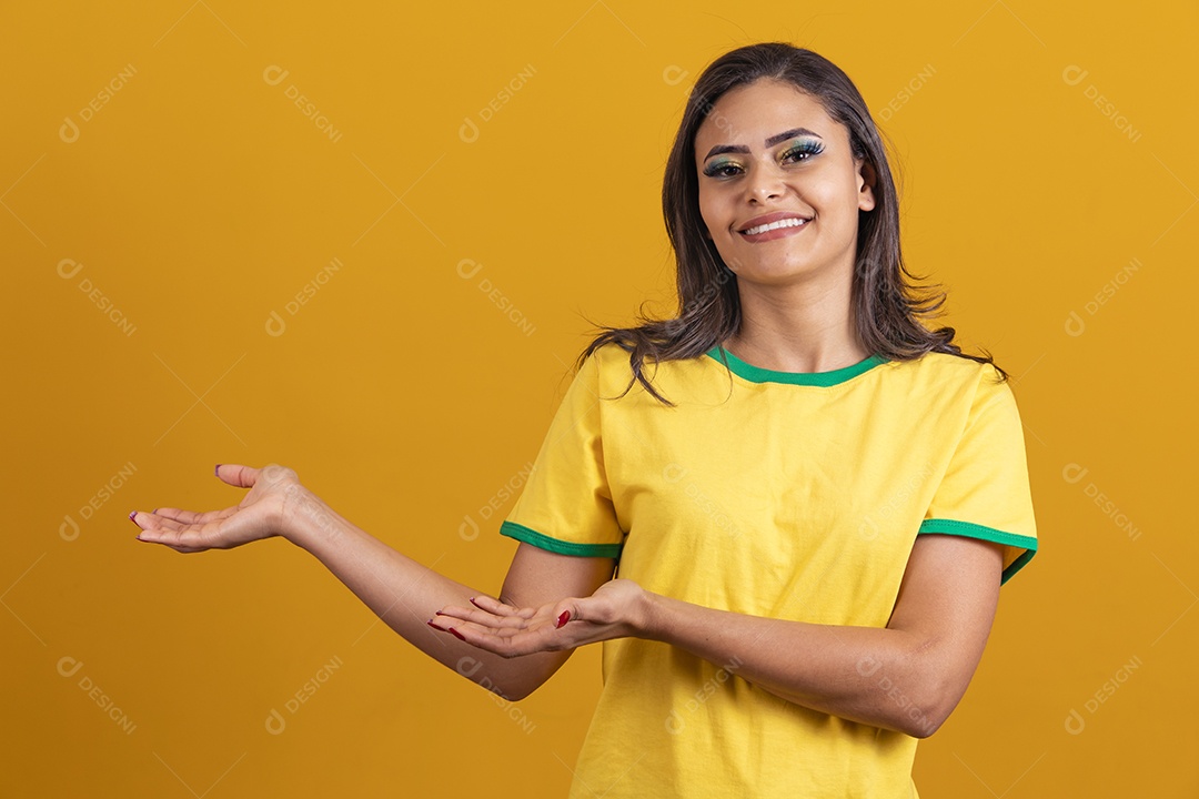 Linda mulher jovem brasileira garota torcedora do brasil fundo amarelo apontando para lado