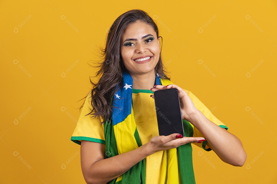 Linda mulher jovem brasileira garota torcedora do brasil segurando celular fundo amarelo