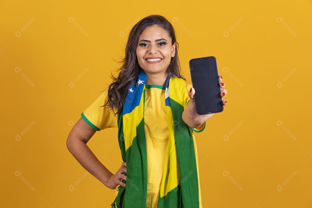 Linda mulher jovem brasileira garota torcedora do brasil segurando celular fundo amarelo