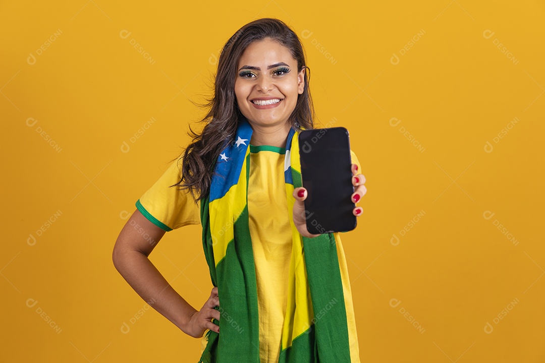 Linda mulher jovem brasileira garota torcedora do brasil segurando celular fundo amarelo