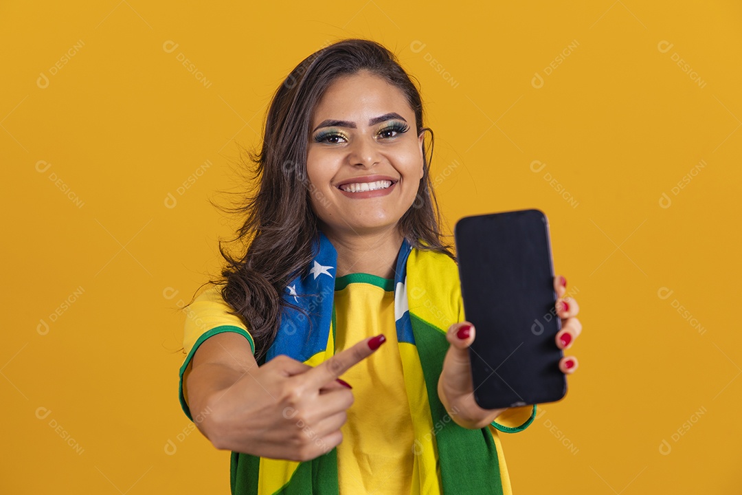 Linda mulher jovem brasileira garota torcedora do brasil segurando celular fundo amarelo