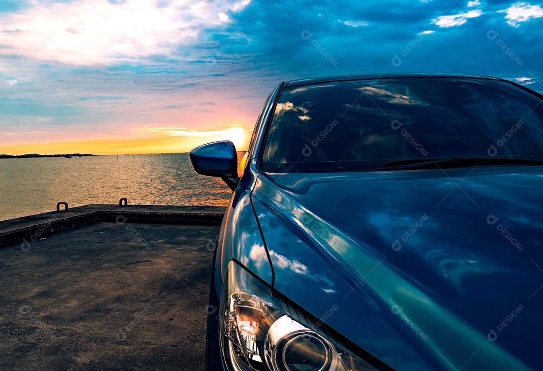 Carro SUV compacto azul com esporte e design moderno estacionado na estrada de concreto à beira-mar ao pôr do sol.