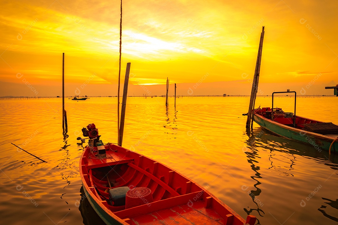Barco do pescador flutuando no mar perto de vara de bambu ao pôr do sol na Tailândia.