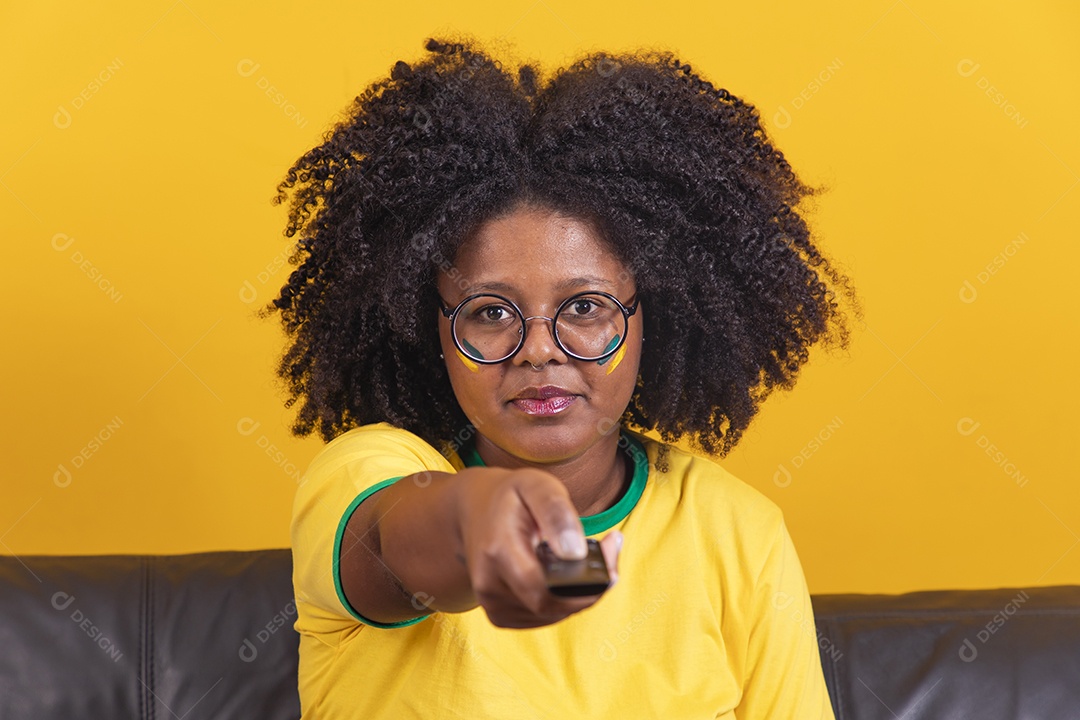 Mulher jovem brasileira torcedora cabelo afro segurando controle da sua televisão para assistir a copa do mundo