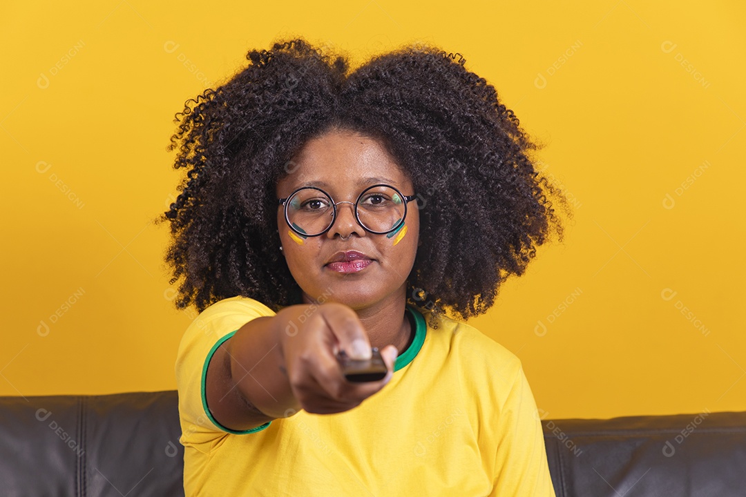 Mulher jovem brasileira torcedora cabelo afro segurando controle da sua televisão para assistir a copa do mundo