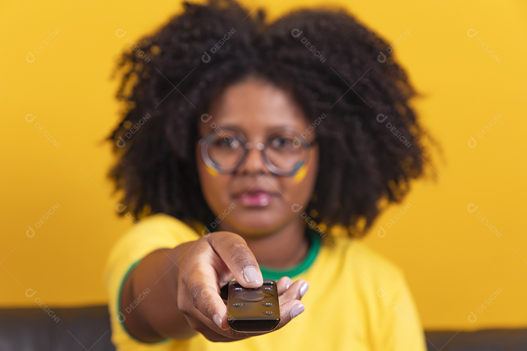 Mulher jovem brasileira torcedora cabelo afro segurando controle da sua televisão para assistir a copa do mundo
