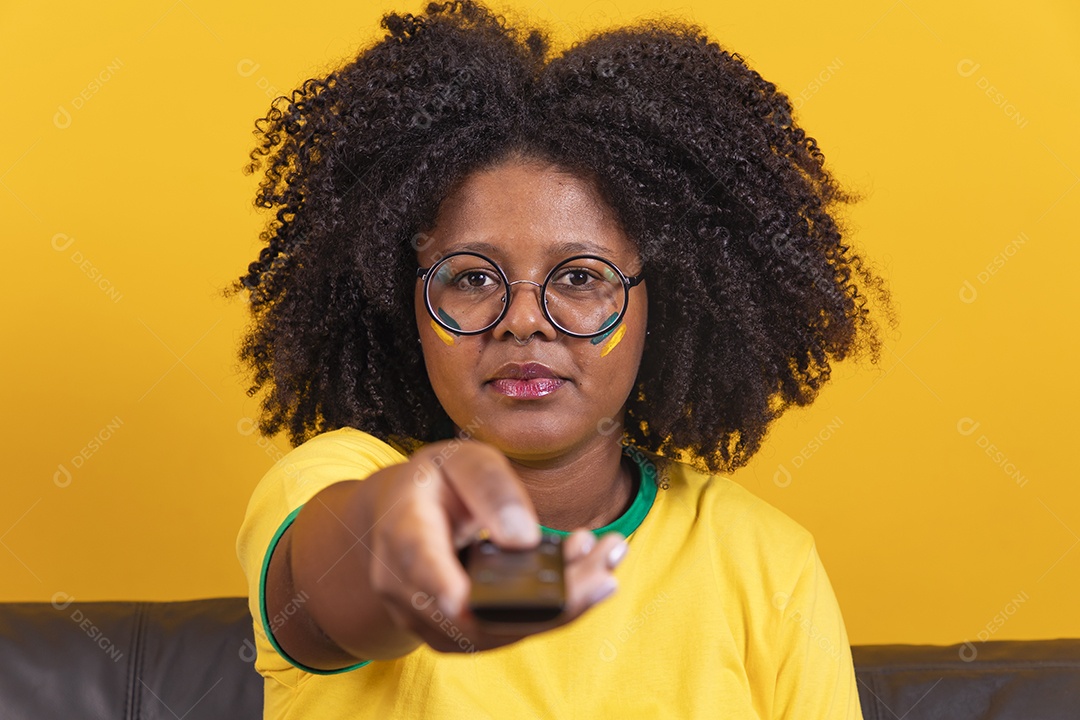 Mulher jovem brasileira torcedora cabelo afro segurando controle da sua televisão para assistir a copa do mundo