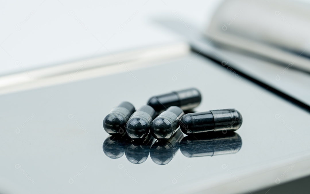 Foco seletivo em pós de carvão ativado na bandeja de drogas de aço inoxidável e desfoque o fundo da cápsula