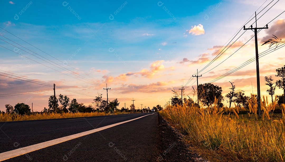 Estrada de asfalto com poste elétrico e prados ao longo do caminho.