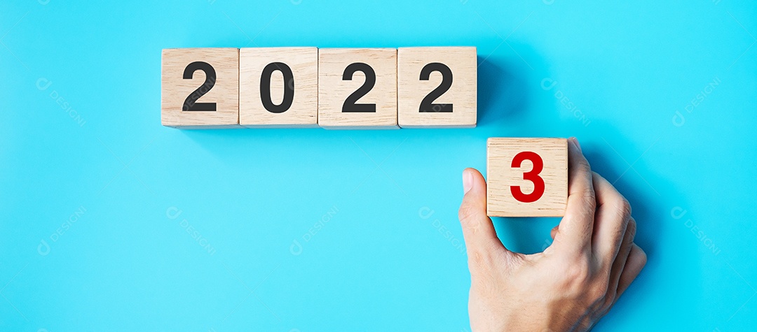 Mão segurando o bloco de cubo de madeira com texto de 2023 em fundo azul.