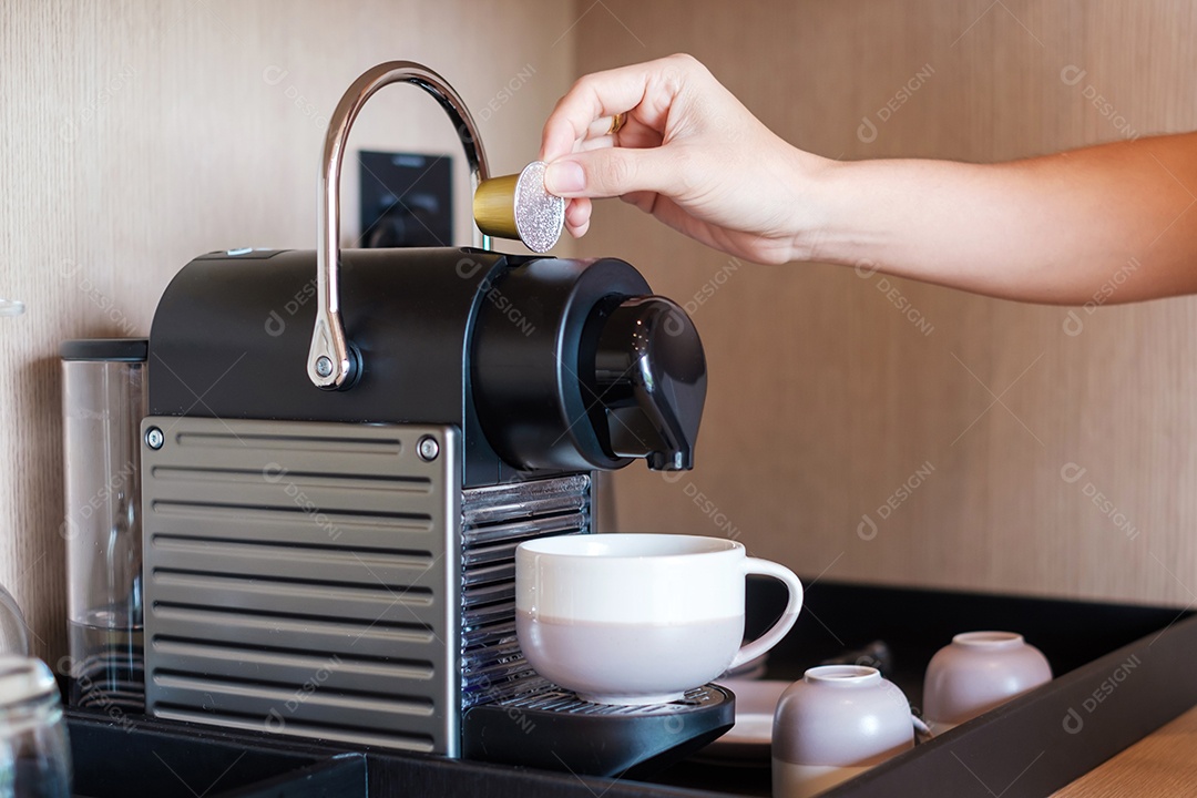 Mão fazendo café expresso por máquina de café com cápsulas na mesa de madeira