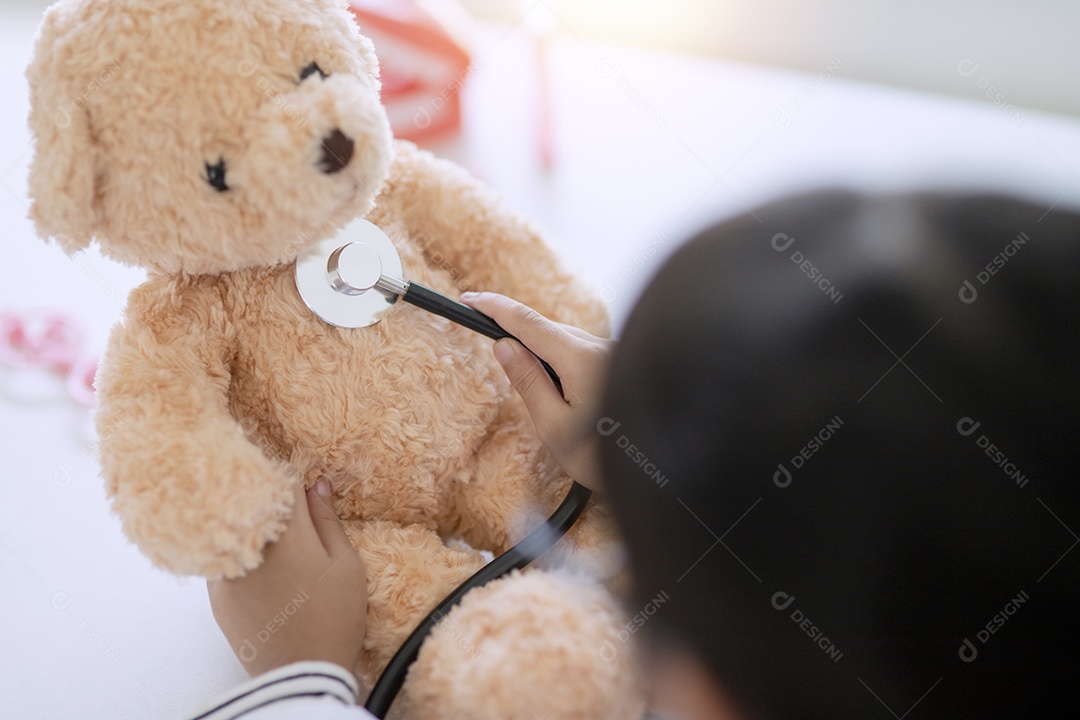 Menina asiática brincando com seu paciente urso de pelúcia em um jogo médico