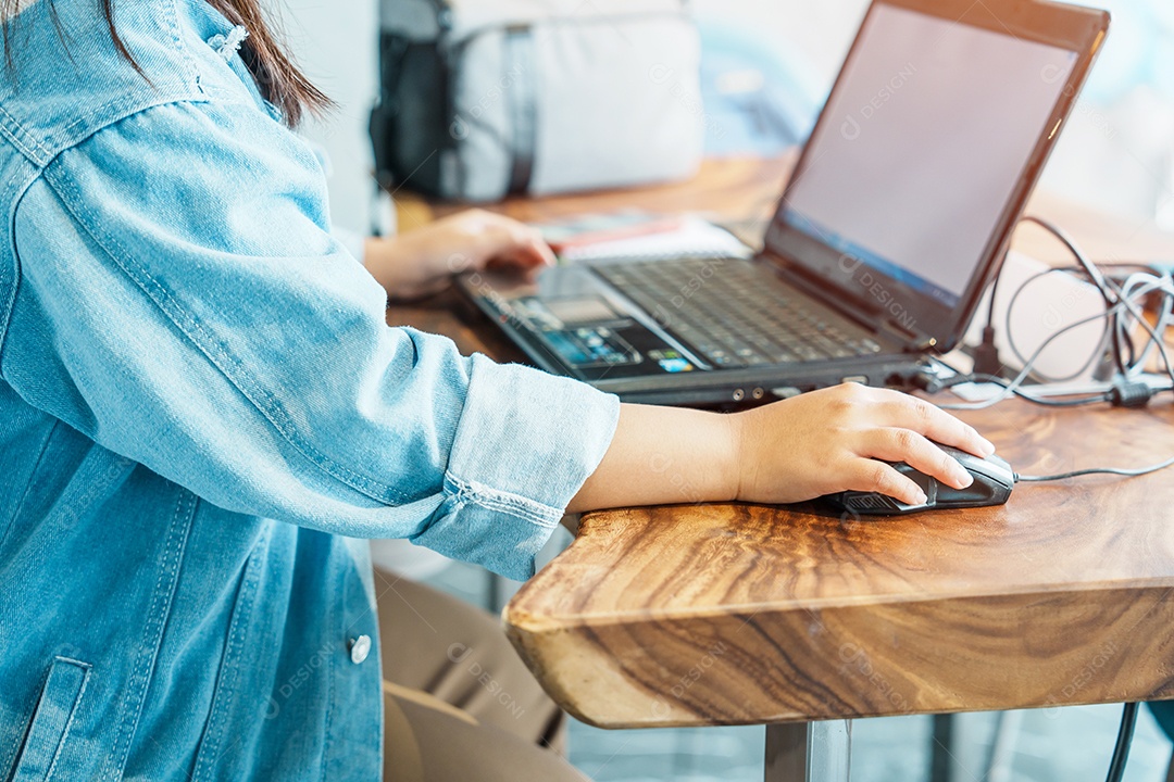 Mão de uma mulher segurando o mouse durante o uso do computador portátil no workpla
