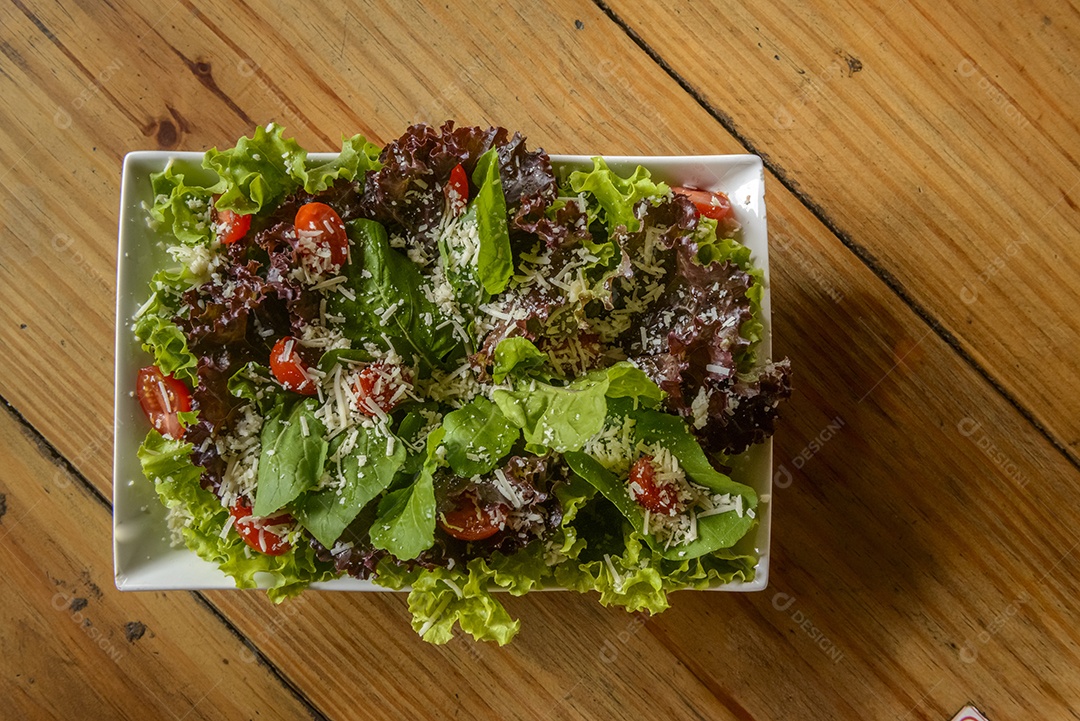 Green salad in white bowl on wooden table.